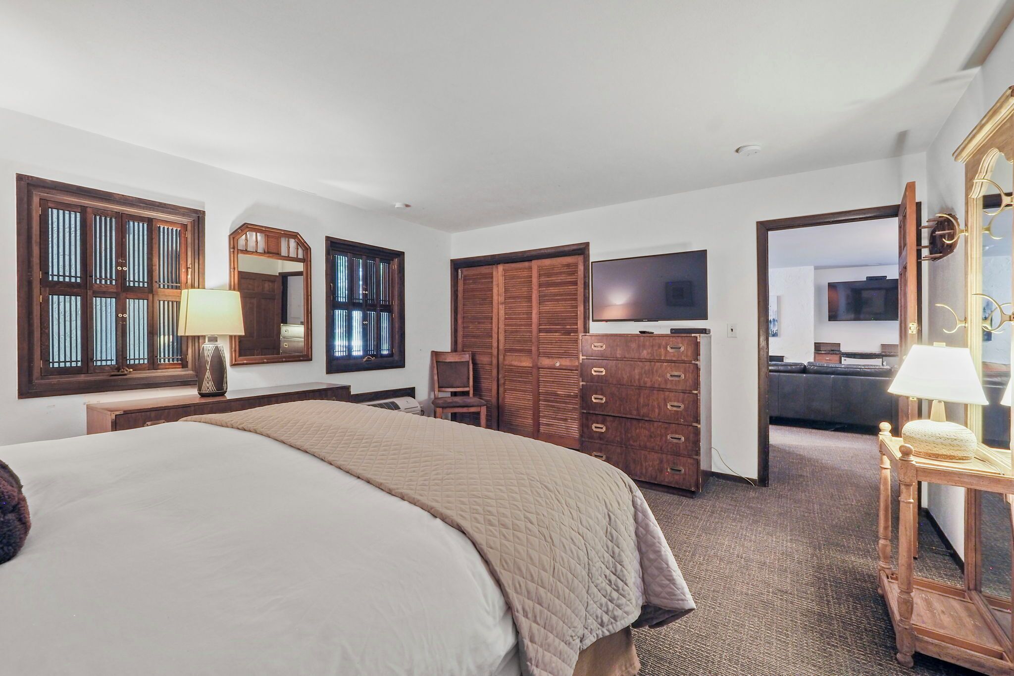 Une chambre d’hôtel avec un grand lit, une armoire en bois, une télévision et un miroir.