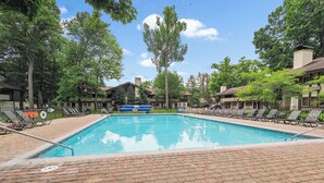 Ein rechteckiger Swimmingpool mit einer Pflasterterrasse, umgeben von Liegestühlen und Bäumen.