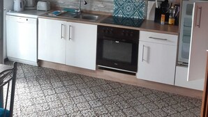 Een compacte keuken met witte kastjes, een ingebouwde oven, een magnetron en een koffiezetapparaat.