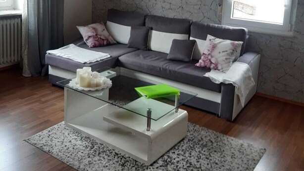 Een moderne woonkamer met een modulaire bank, een glazen salontafel en een wand met een stenen patroon.