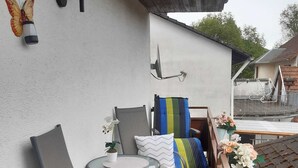 Een balkon met een tafel, stoelen, een decoratieve vlinder en een wandlamp.