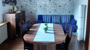 Een eetgedeelte met een houten tafel, stoelen, een blauwe bank en een behang met patroon.