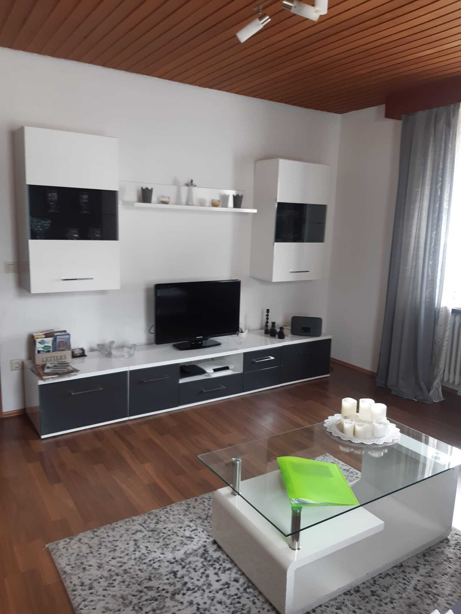 A modern living room with a flat-screen TV, built-in cabinets, and a glass coffee table.