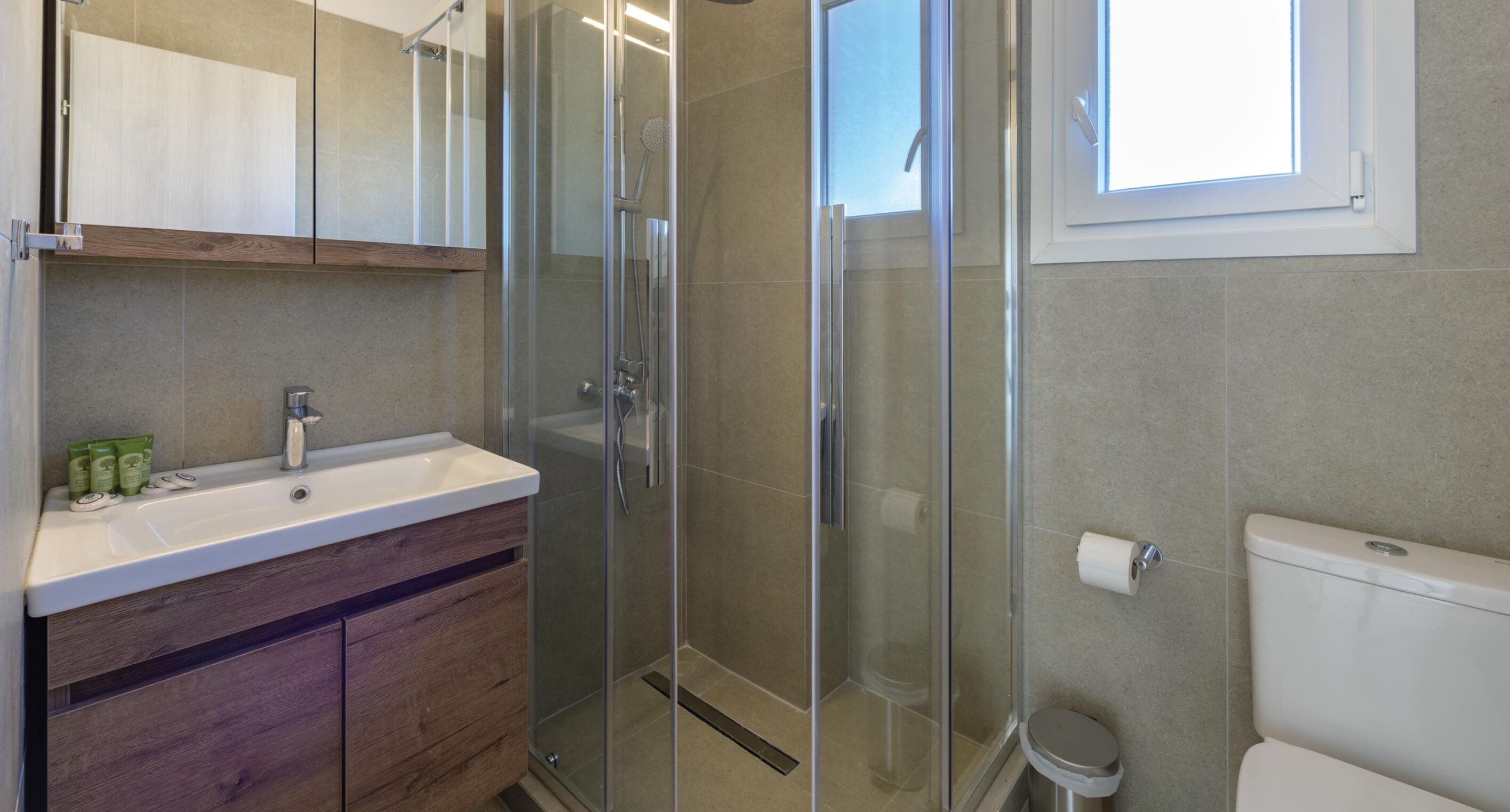 Un baño moderno con cabina de ducha de vidrio, un lavamanos blanco y un inodoro.