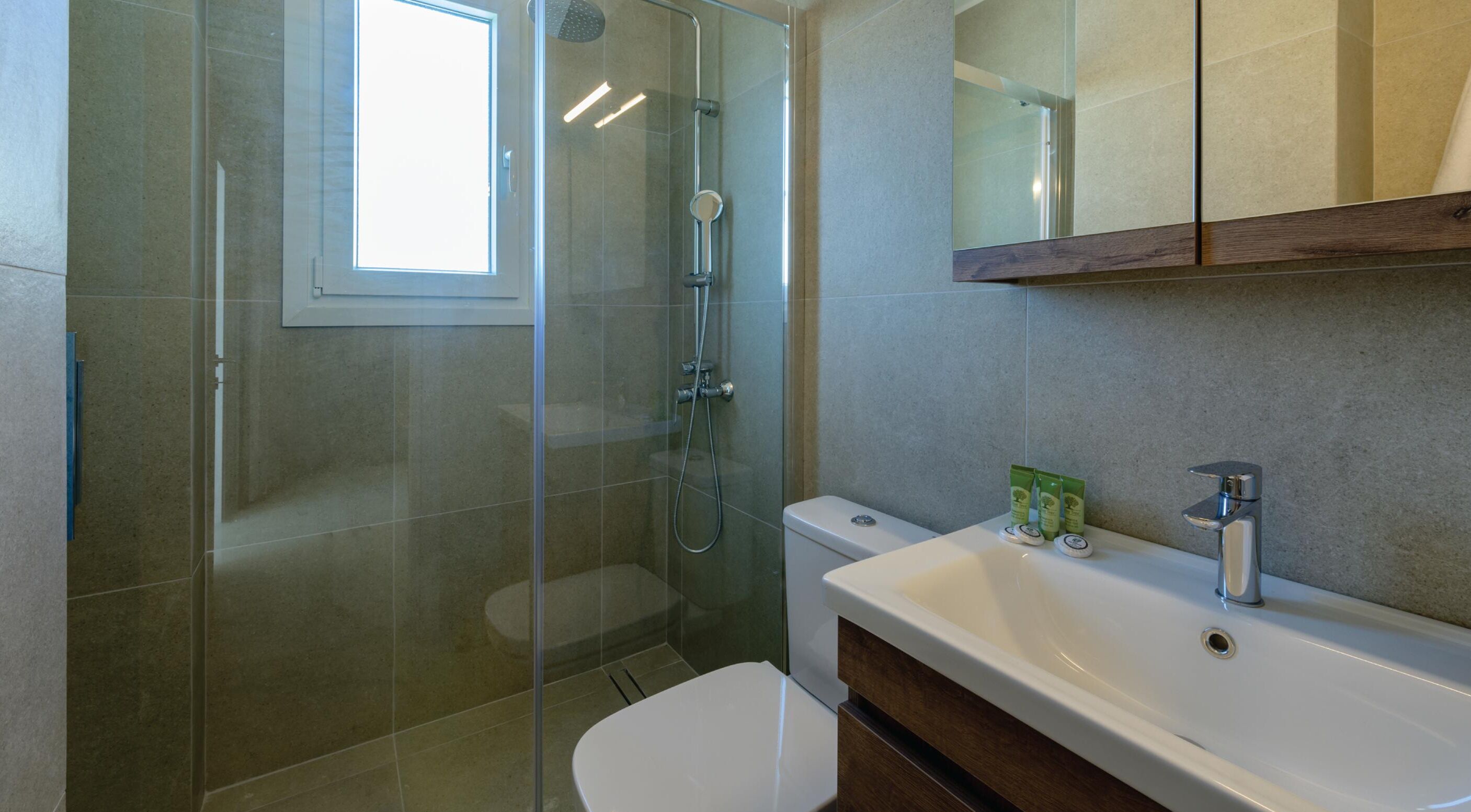 Un baño moderno con cabina de ducha de vidrio, inodoro, lavamanos con espejo y ventana que proporciona luz natural.