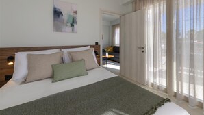 A hotel room with a large bed, a wooden headboard, a green throw blanket, and a view of the outdoors through sheer curtains. - Komos Villas by Airstay (Spata-Artemida)