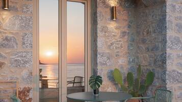 A stone wall with a glass door leading to a balcony overlooking a sunset over the sea.