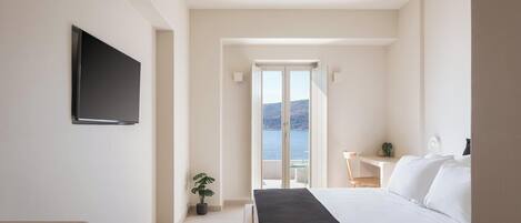 Un dormitorio con cama, televisión, una mesita con una planta y vistas al mar a través de un ventanal.