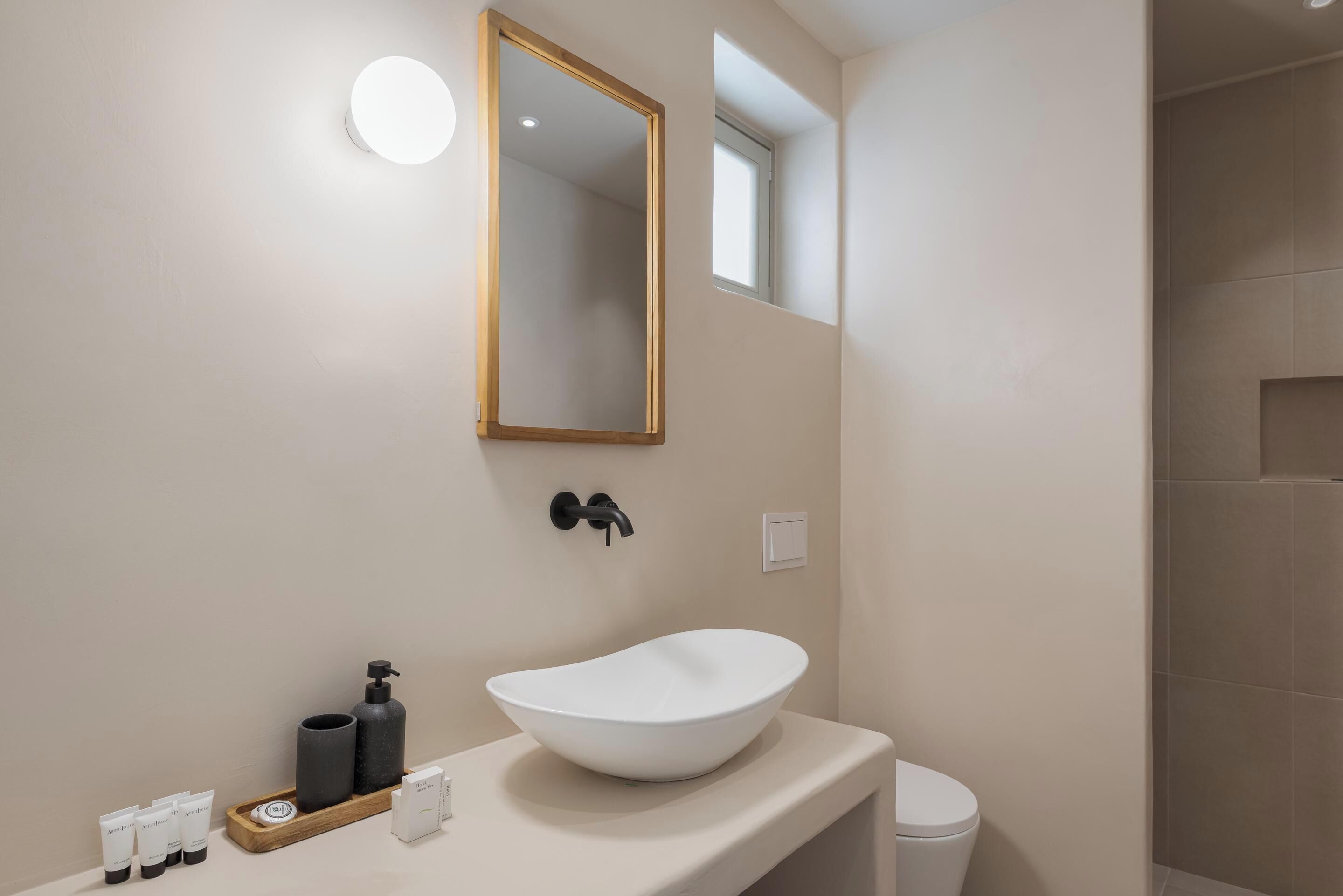 A modern bathroom with a white vessel sink, a round mirror, and a small window.