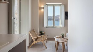 Een balkon met uitzicht op zee, een rieten stoel, een klein rond tafeltje en een aan de muur bevestigde televisie.