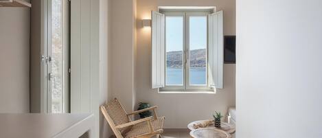 A balcony with a view of the sea, a wicker chair, a small round table, and a wall-mounted TV.