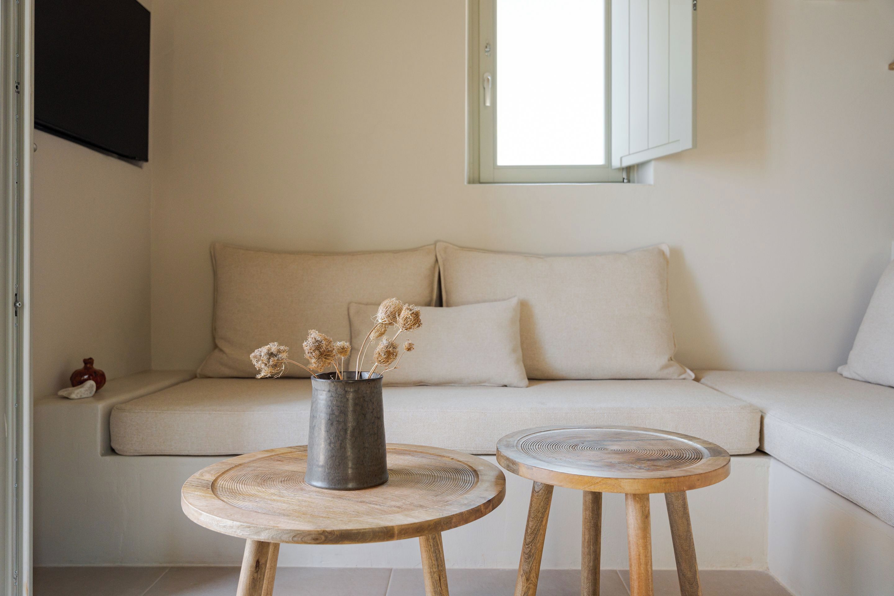 A minimalist living room with a sofa, two wooden side tables, and a vase with dried flowers.