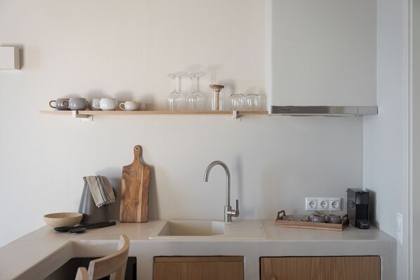 A modern kitchen with a wooden countertop, a sink, and a shelf above holding glassware and cups. - Yerma Suites Limeni (East Mani)