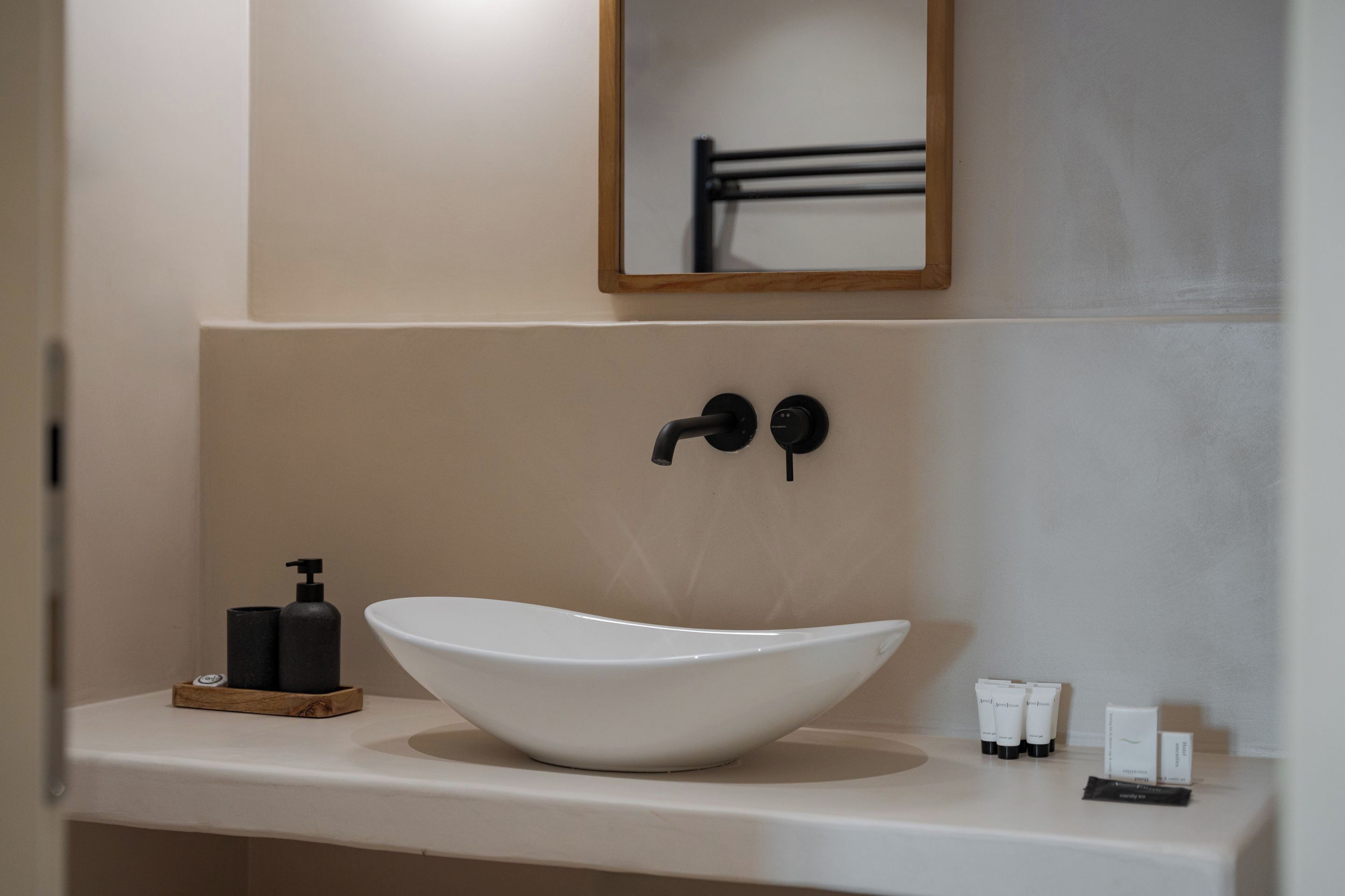 Un baño con un lavabo blanco de diseño, dosificador de jabón negro y artículos de aseo en la encimera.