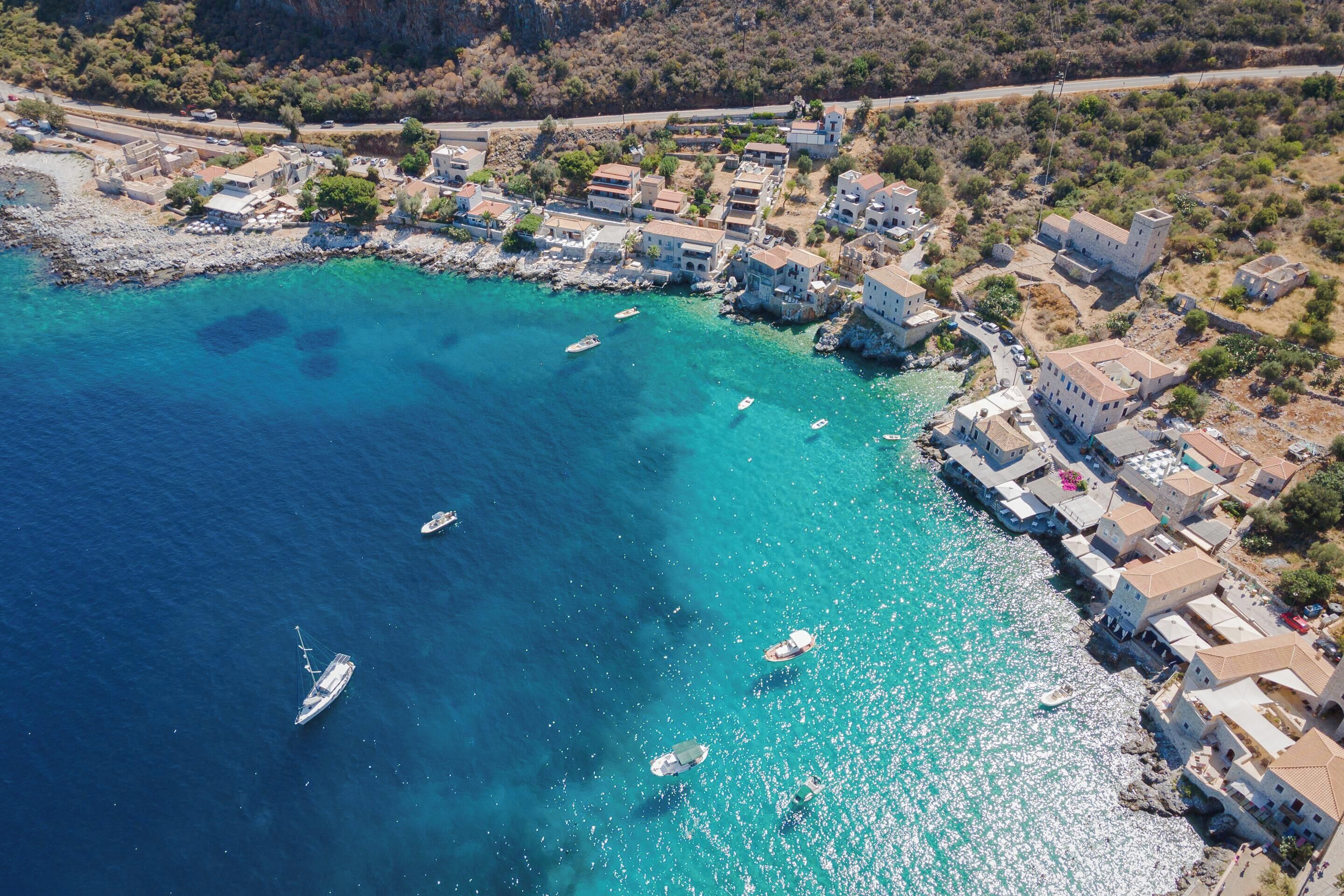 An aerial view of a coastal village with buildings along the shoreline and boats in the water.