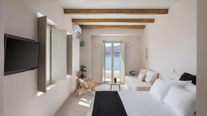 Een slaapkamer met een bed, een televisie, een balkon met uitzicht en een zithoek met een tafel en stoelen.