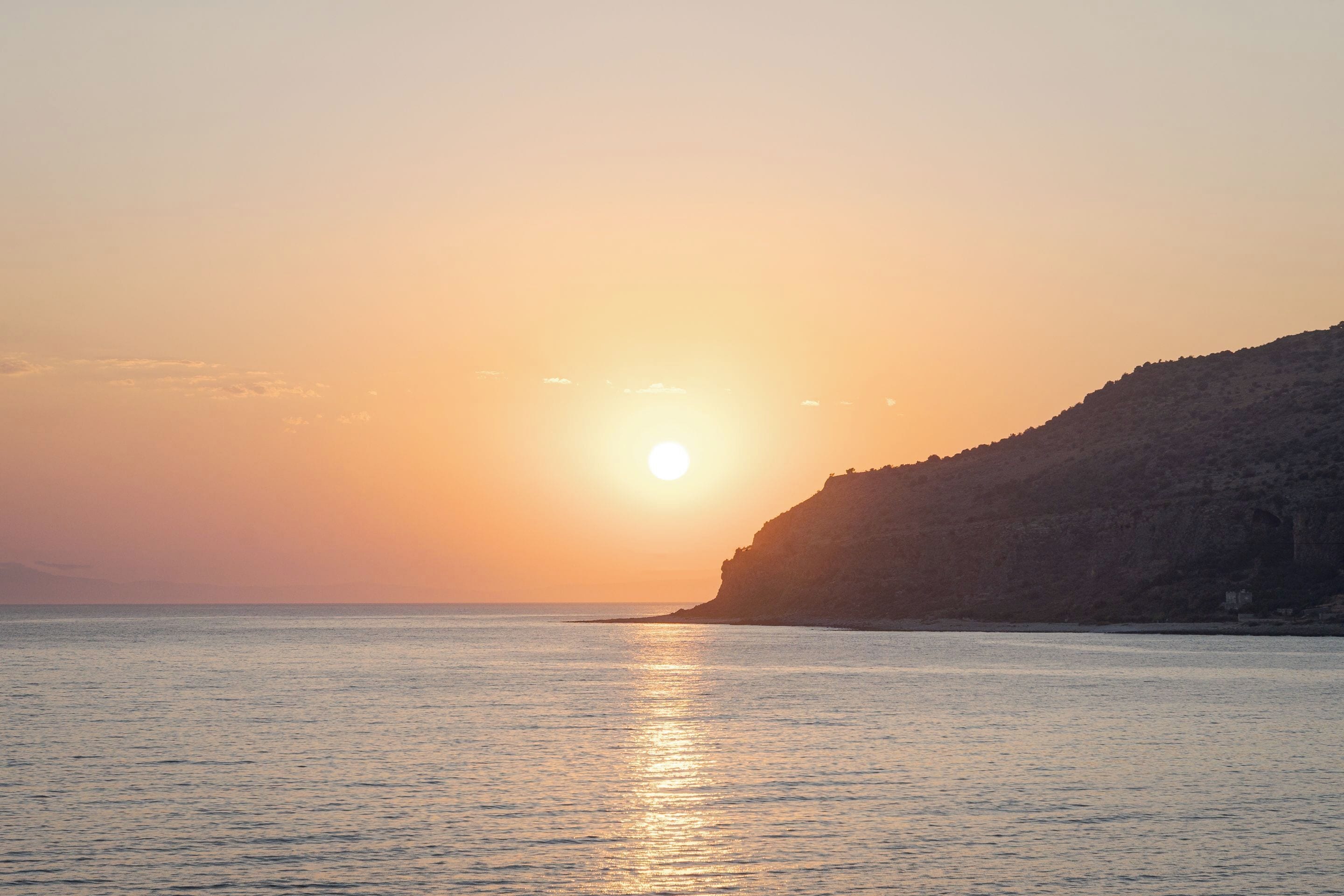 A sunset over a calm sea with a rocky coastline.