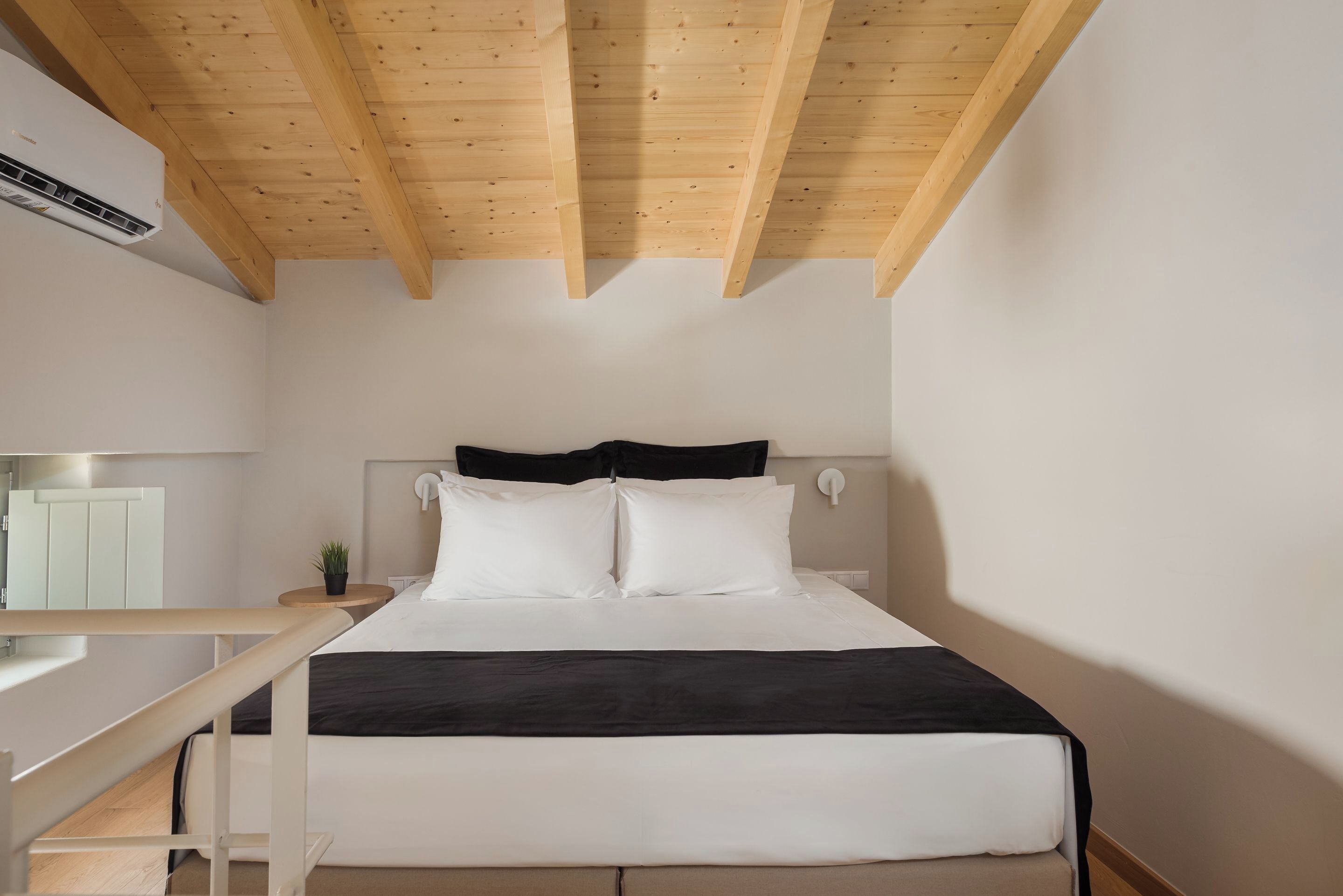 Une chambre à coucher avec un lit, des poutres en bois au plafond, une table de chevet et une petite plante.