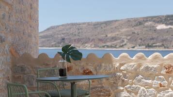 A stone wall with a table and chairs, overlooking a body of water and a hilly landscape.