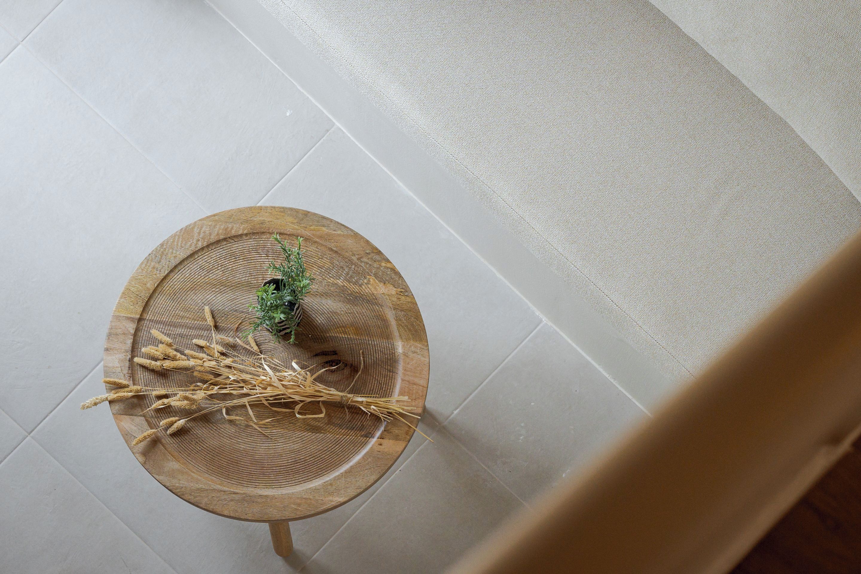 A top-down view of a room with a wooden table featuring a woven basket, wheat stalks, and a small plant.