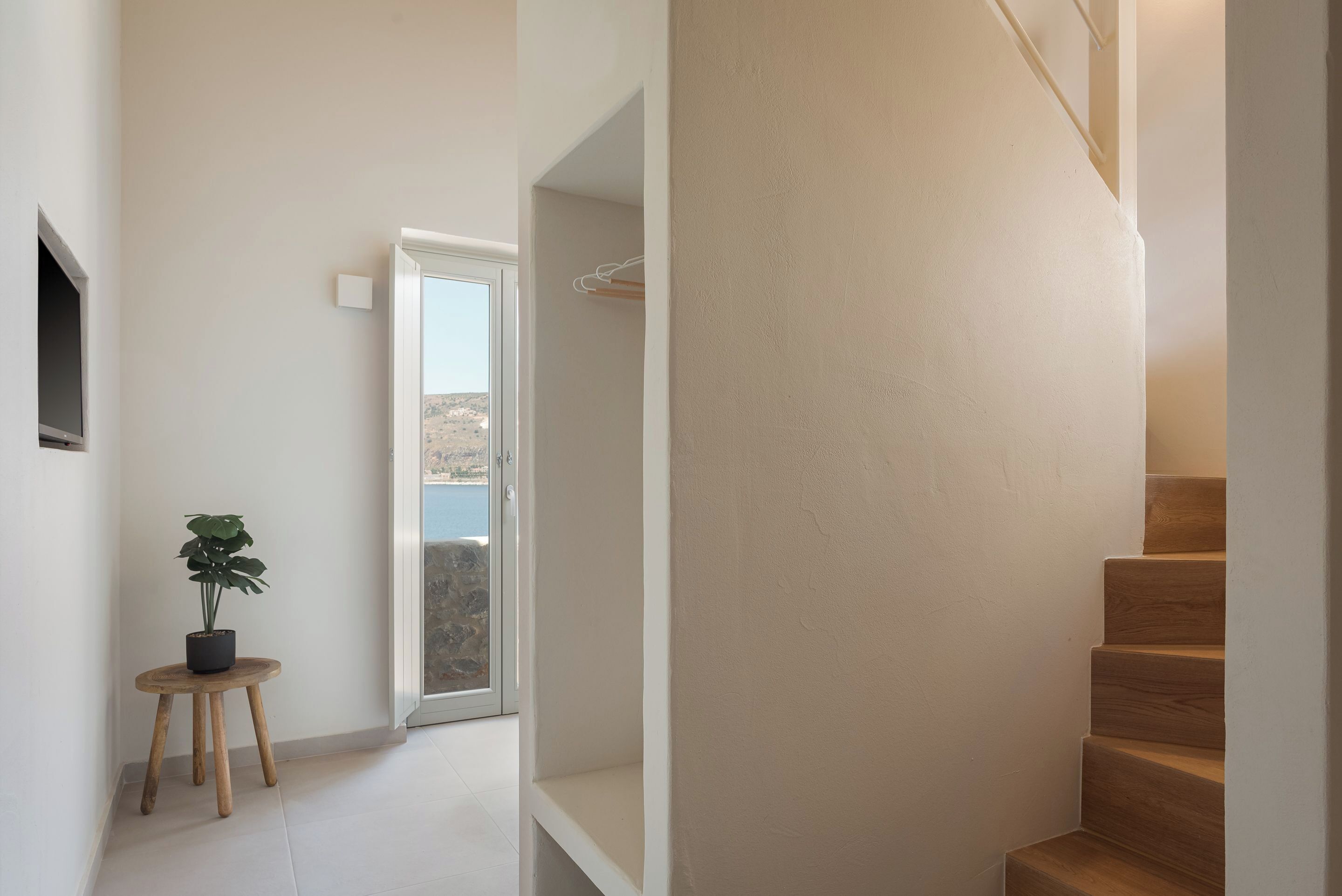 A staircase with a wooden finish, a small wooden stool with a potted plant, and a door leading to a balcony with a view of the outdoors.