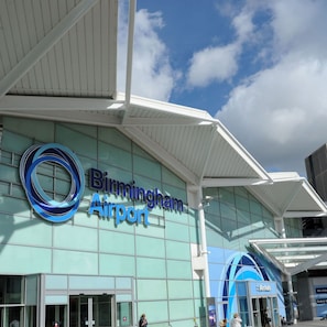 Exterior del Aeropuerto de Birmingham con cielo despejado y un gran logo circular en la fachada.