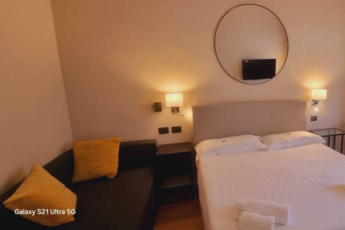 A hotel room with a bed, two bedside tables, a desk, a chair, and a large mirror.
