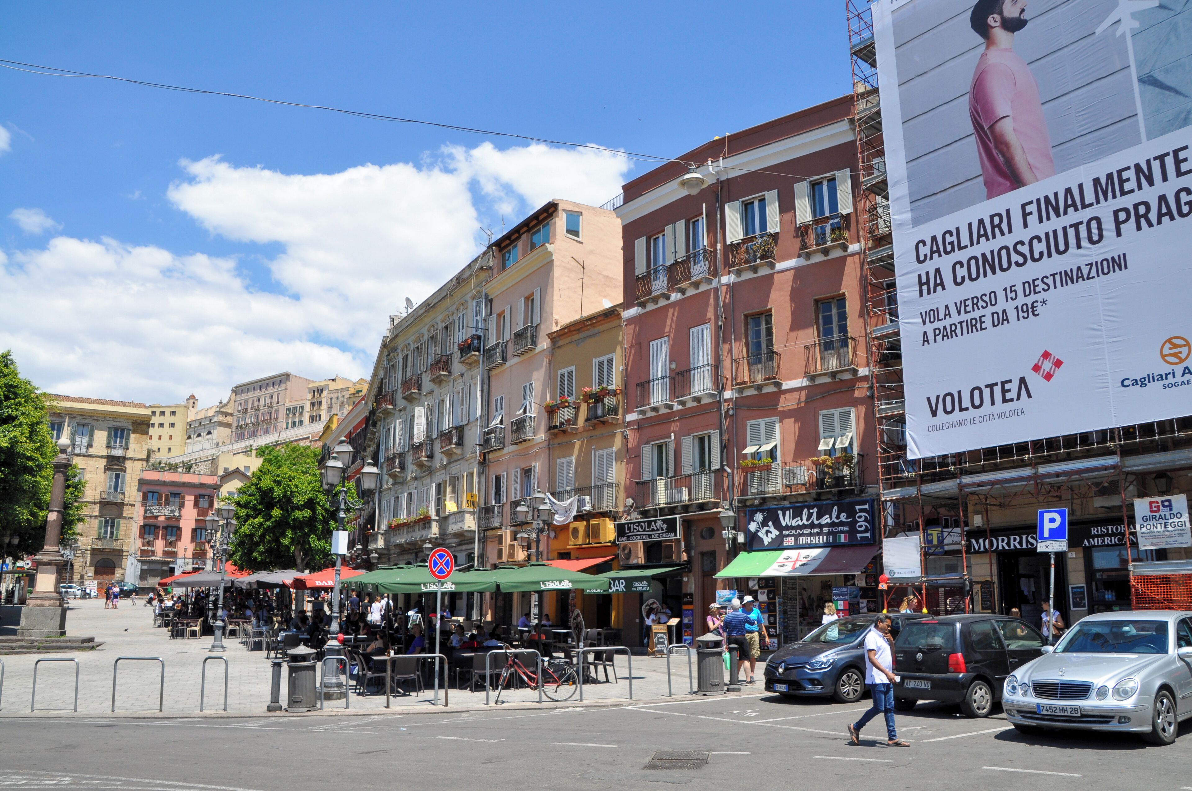 A street with cafes, shops, and a large billboard advertising a travel service.