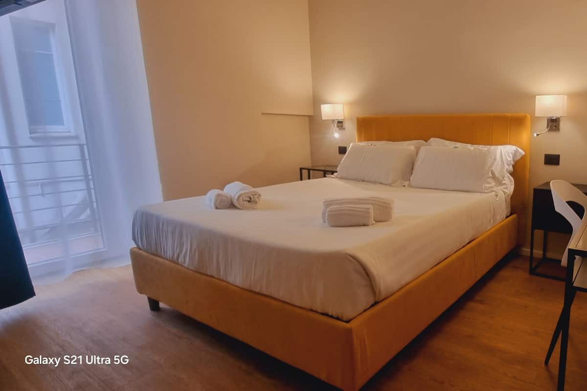 A hotel room with a bed, bedside tables, a desk, and a lamp.