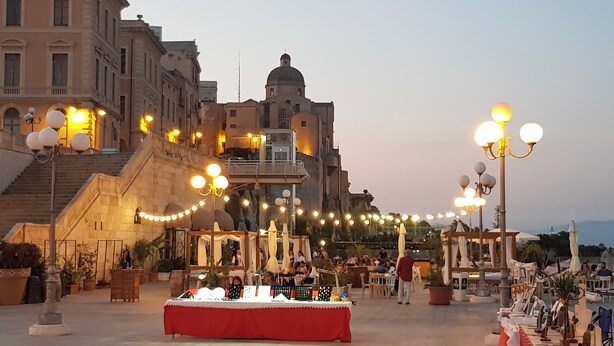 Um terraço com área de estar ao ar livre, uma mesa com objetos e uma escadaria que leva a um edifício.