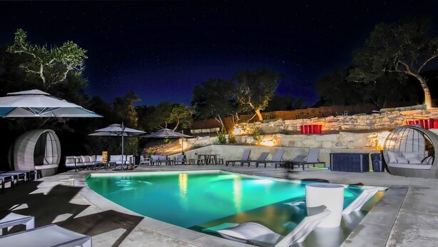 A swimming pool with lounge chairs and umbrellas, surrounded by stone walls and trees.