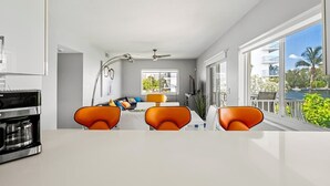 A modern kitchen with a coffee maker, orange chairs, and a dining area with a view of the outdoors. - Waterfront Retreat with Pool & Steps to Beach (Pompano Beach)