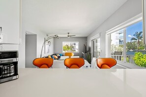 Una cocina moderna con cafetera, sillas anaranjadas y un comedor con vistas al exterior.