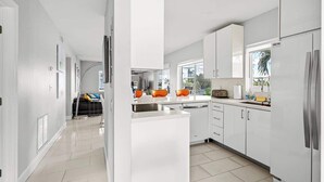 A modern kitchen with white cabinetry, a central island, and a large refrigerator. - Waterfront Retreat with Pool & Steps to Beach (Pompano Beach)