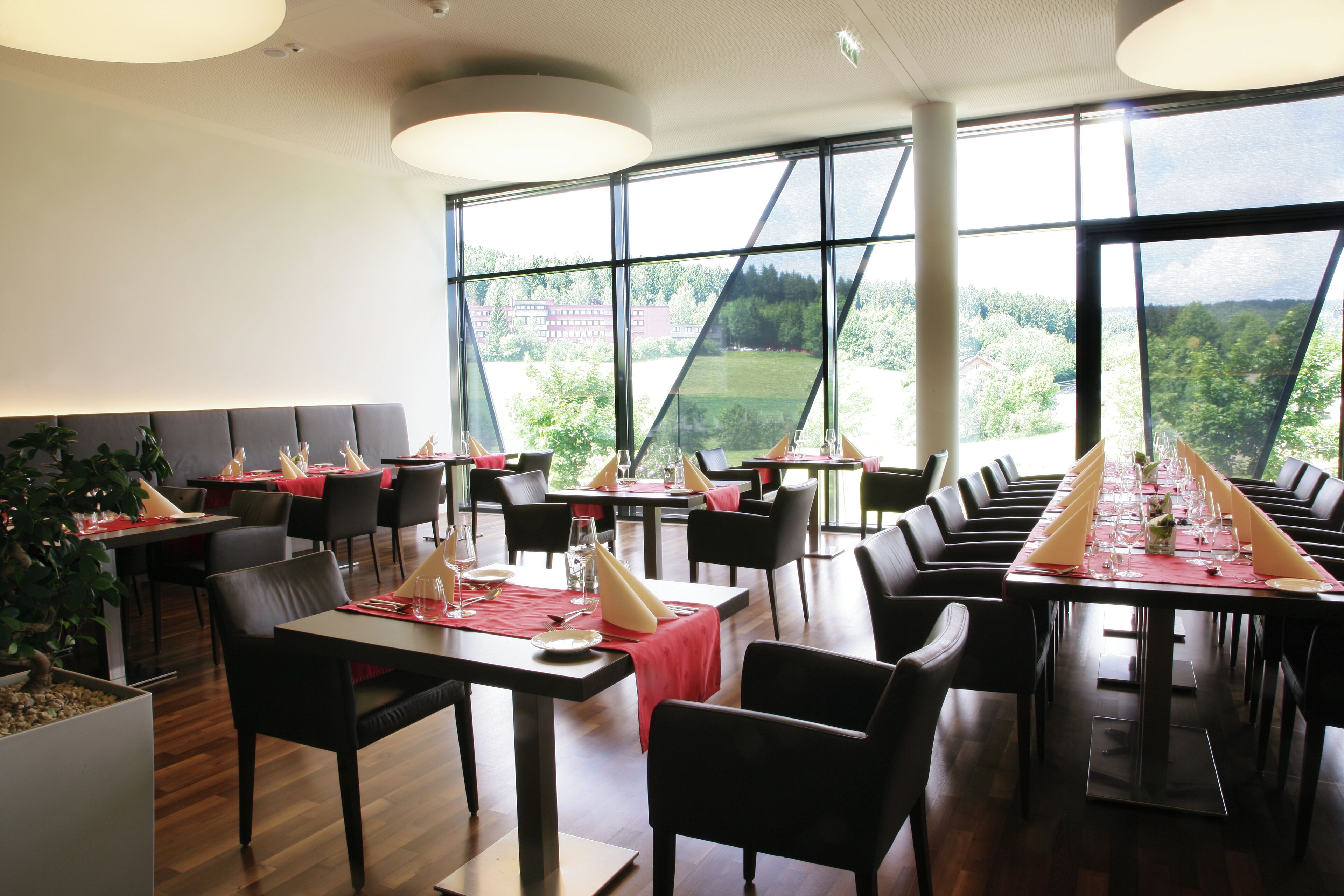 Un restaurant amb taules llargues preparades per dinar, grans finestres que ofereixen vista a l'exterior i una decoració interior moderna.