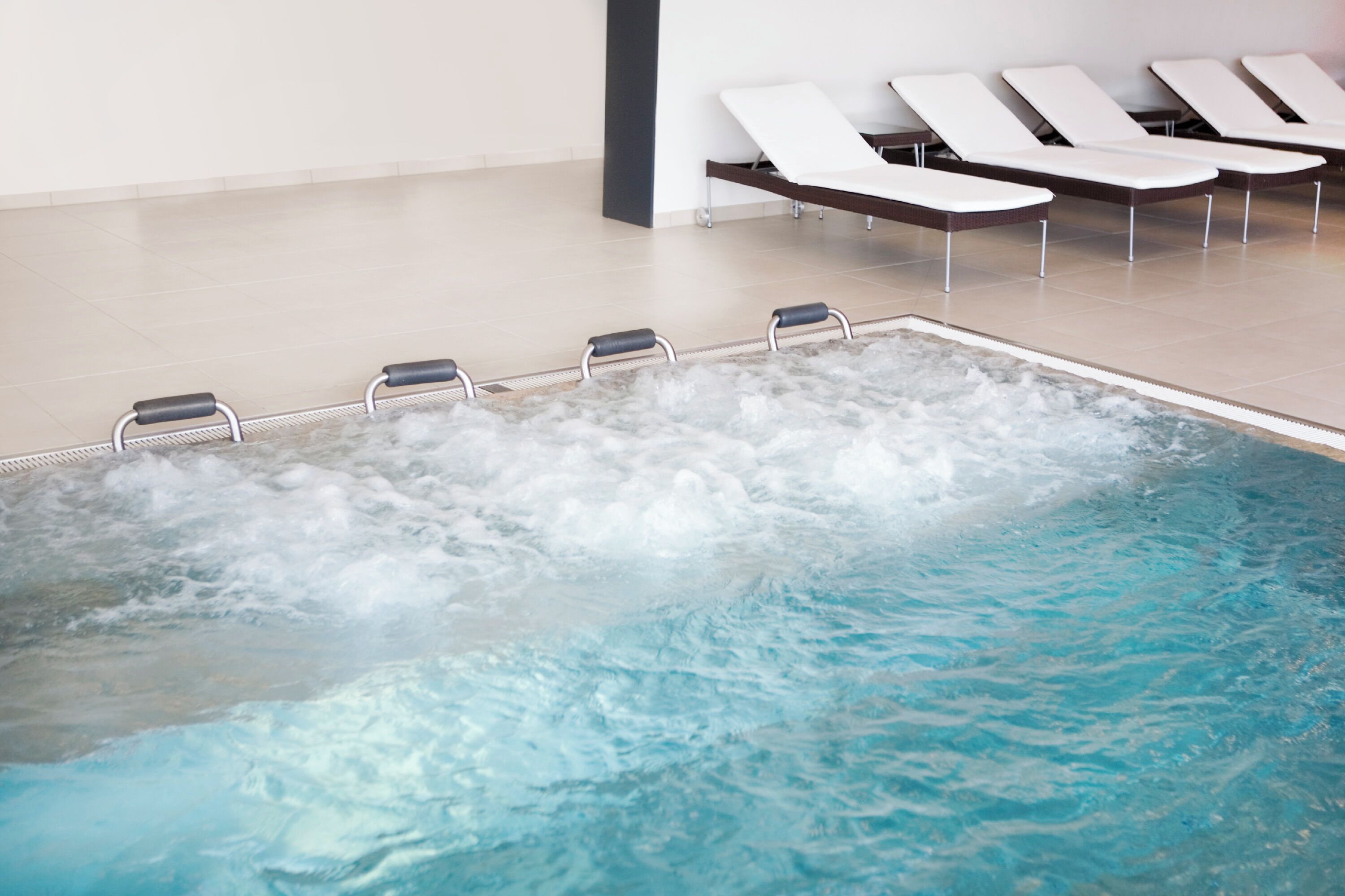 A swimming pool with a hot tub area, lounge chairs, and a tiled floor.