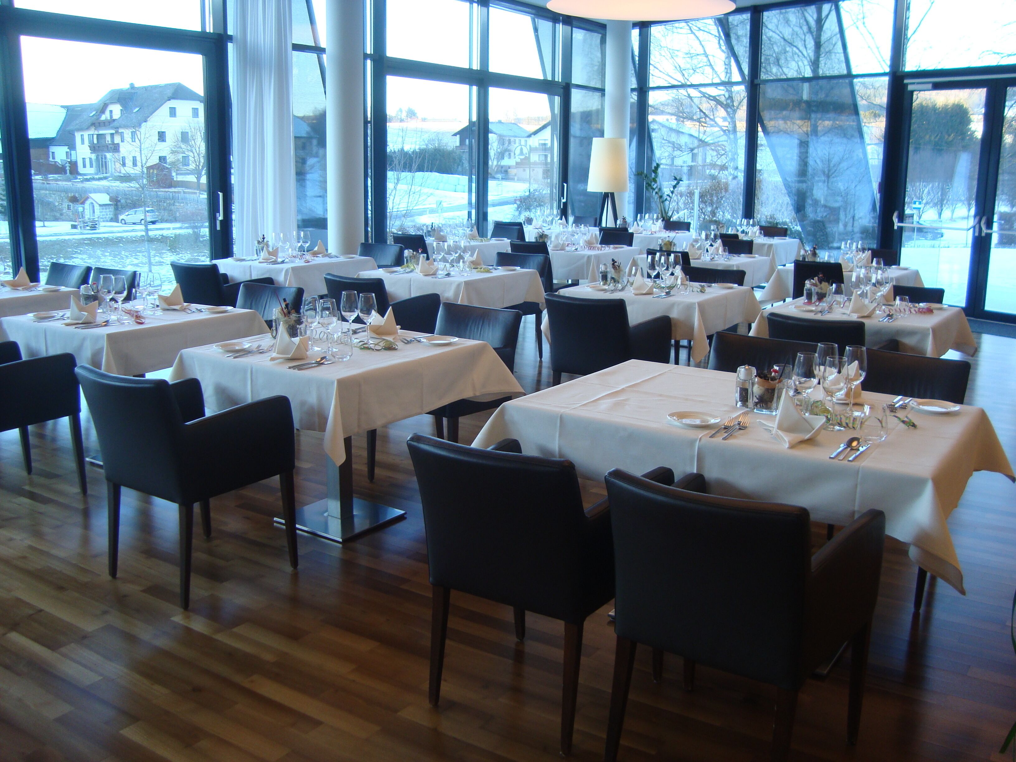 A restaurant with multiple tables set for dining, large windows, and a view of the outside.