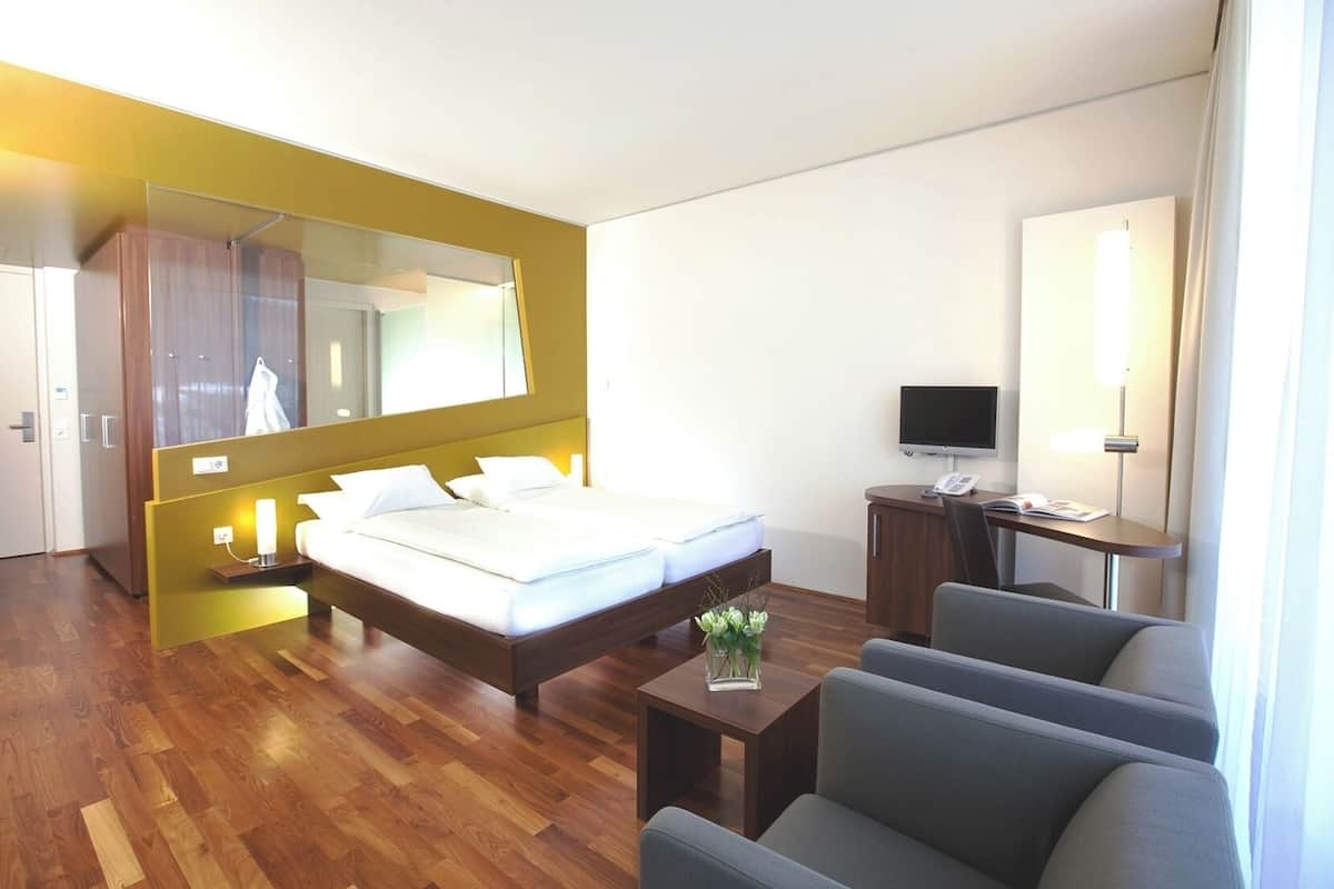 Moderni hotellihuone, jossa on suuri sänky, työpöytä tuolilla, televisio ja peili.