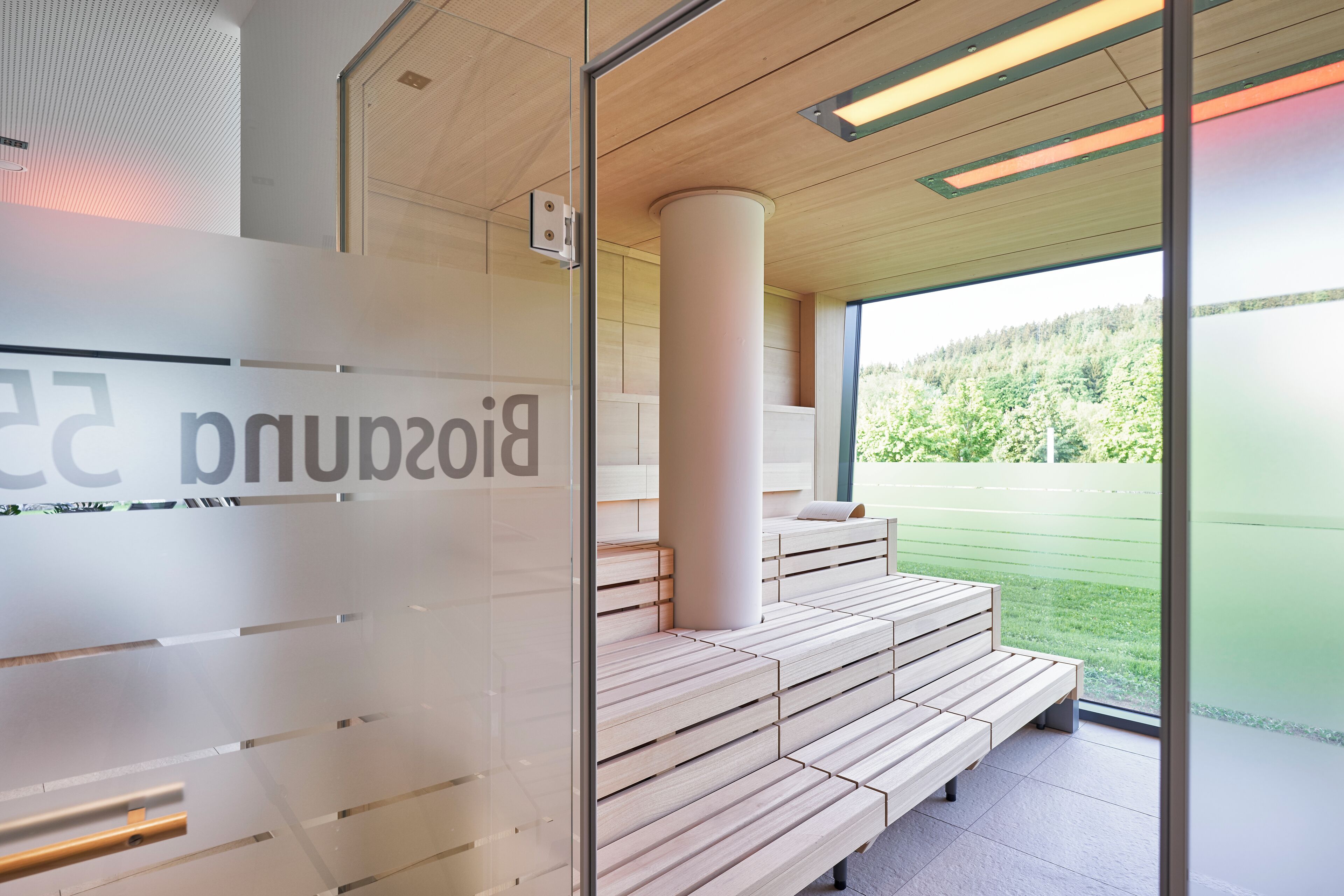 A modern indoor seating area with tiered wooden benches and a glass wall with a partial view of greenery outside.