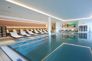 Una piscina interior moderna con sillas de descanso y zona de spa.