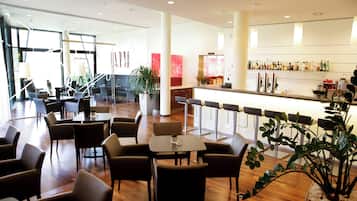 En modern hotellobby med en bardel, sittgrupper och stora fönster.