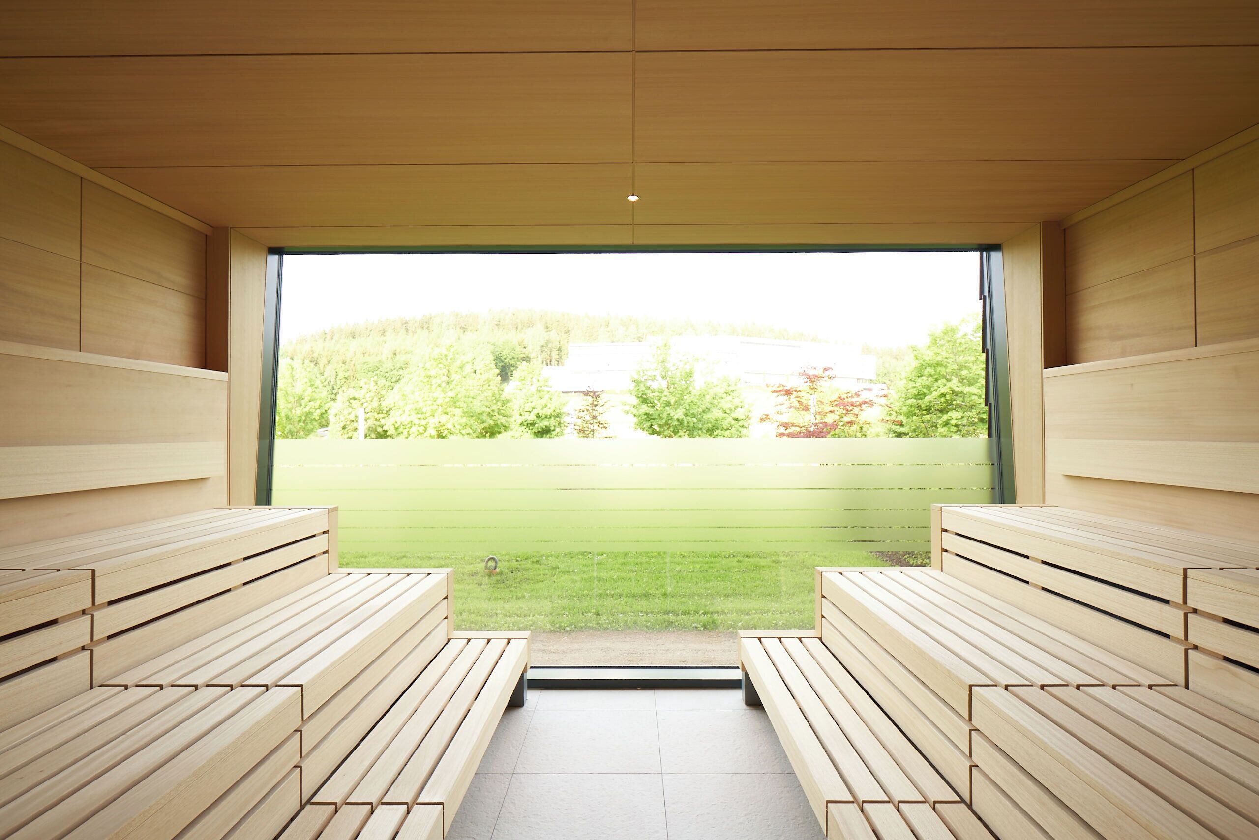 Uma sauna com bancos de madeira e vista para um gramado verde e árvores.