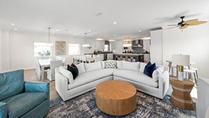 A spacious living room with a large L-shaped sectional sofa, a round coffee table, and a dining area with a white table and chairs. - Papa’s Beach House | 11BR/11.5BA Gulf Shores | Private Pool Coastal Escape (Gulf Shores)