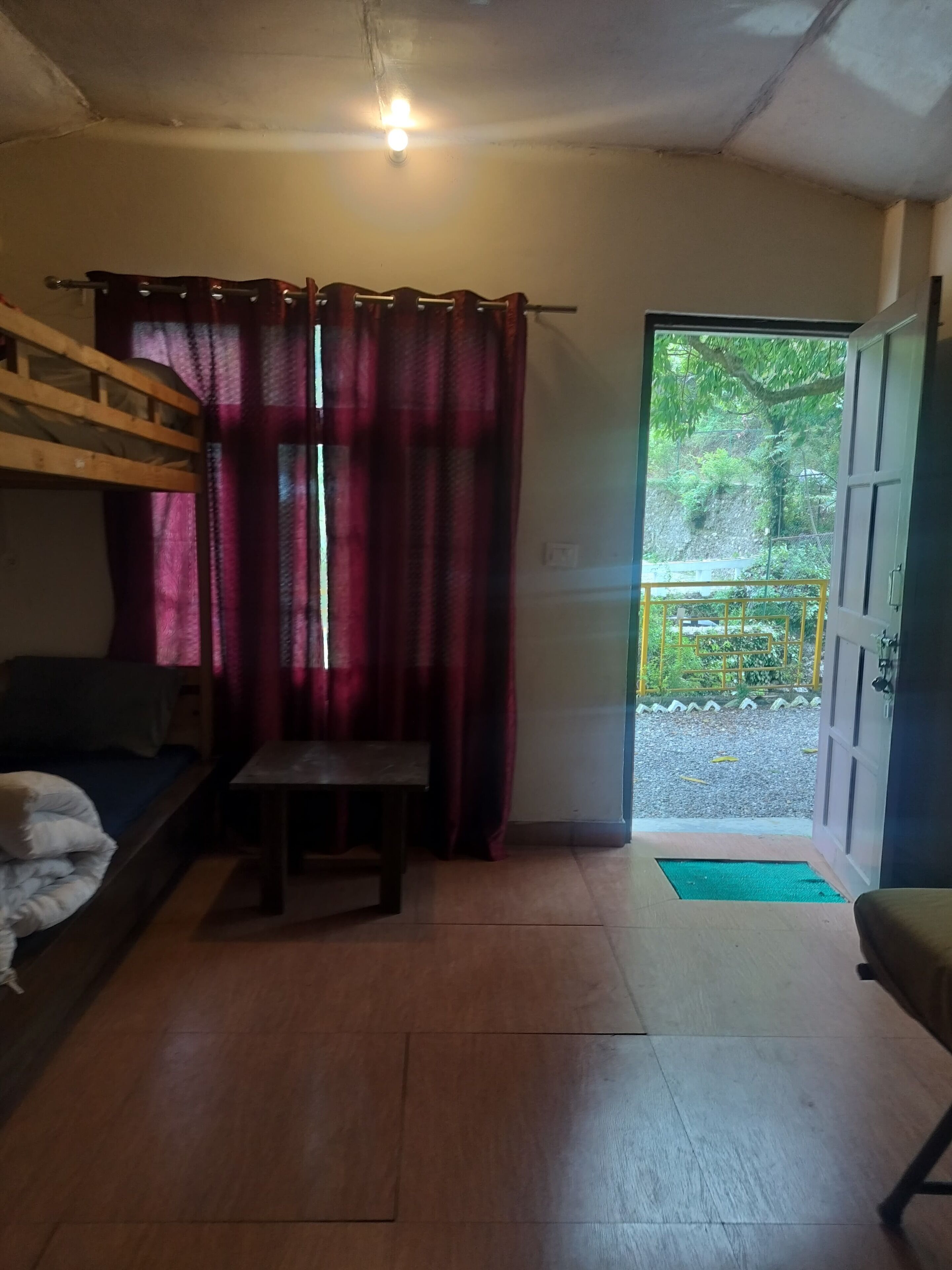 A room with a bunk bed, a small table, a chair, and a door leading to an outdoor area.