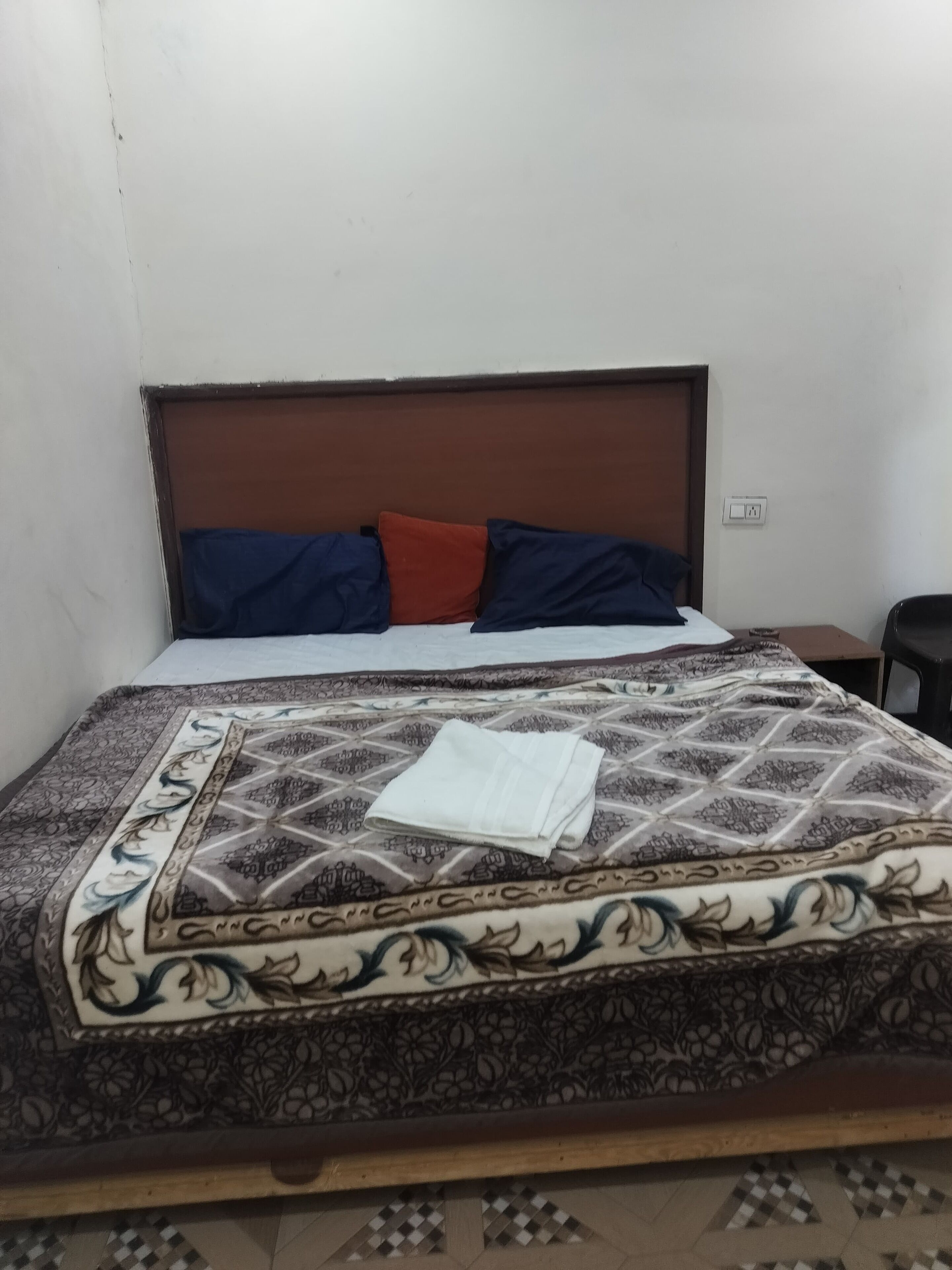 Un lit bien fait, avec une couvre-lit à motifs, deux oreillers et une serviette blanche pliée.