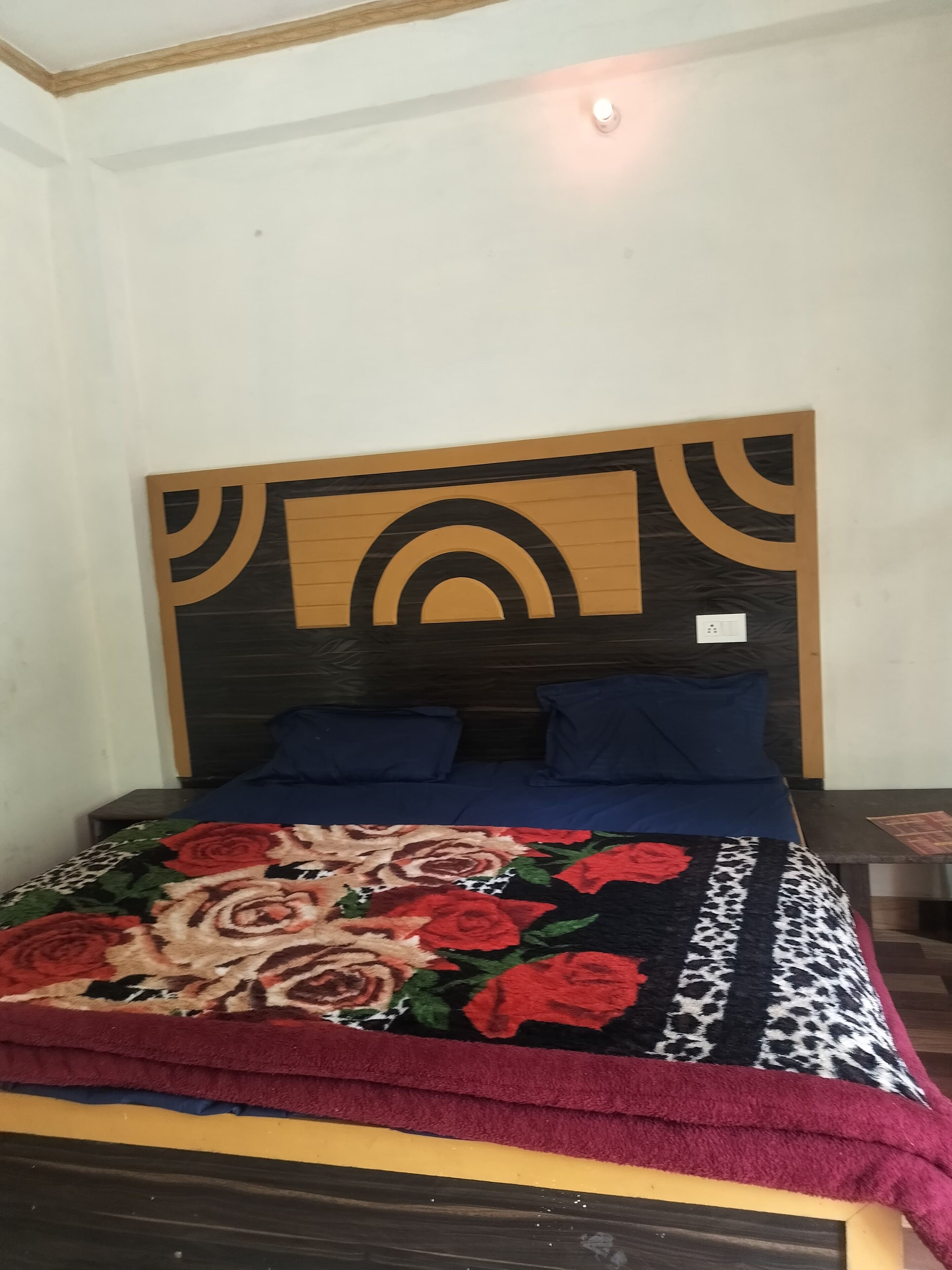 A bed with a floral bedspread, two blue pillows, and a headboard with a geometric design.