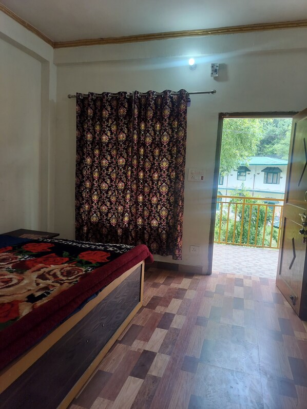 A bedroom with a bed, patterned curtains, a checkered floor, and a view of a balcony with a railing.