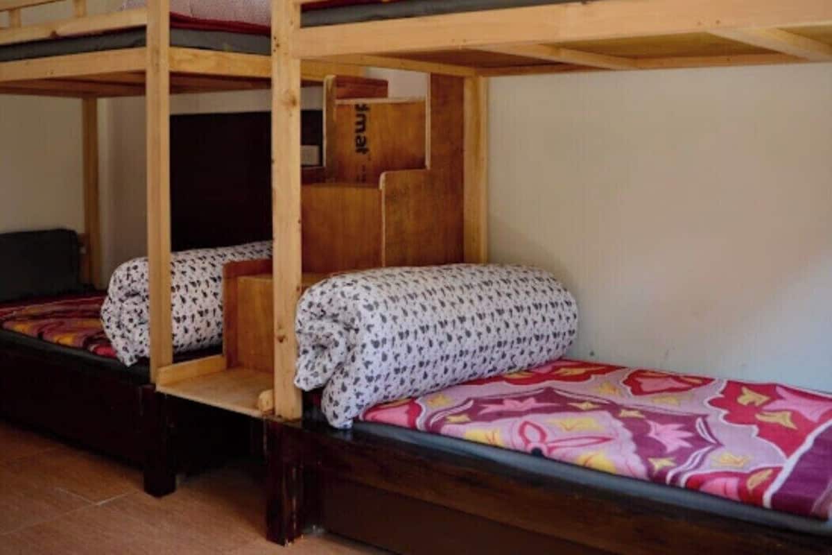 A dormitory room with bunk beds, a wooden wardrobe, and a small desk.