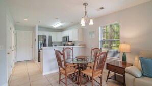 Una cocina moderna con armarios blancos, una isla central y una zona de comedor con sillas de madera y una mesa de vidrio.