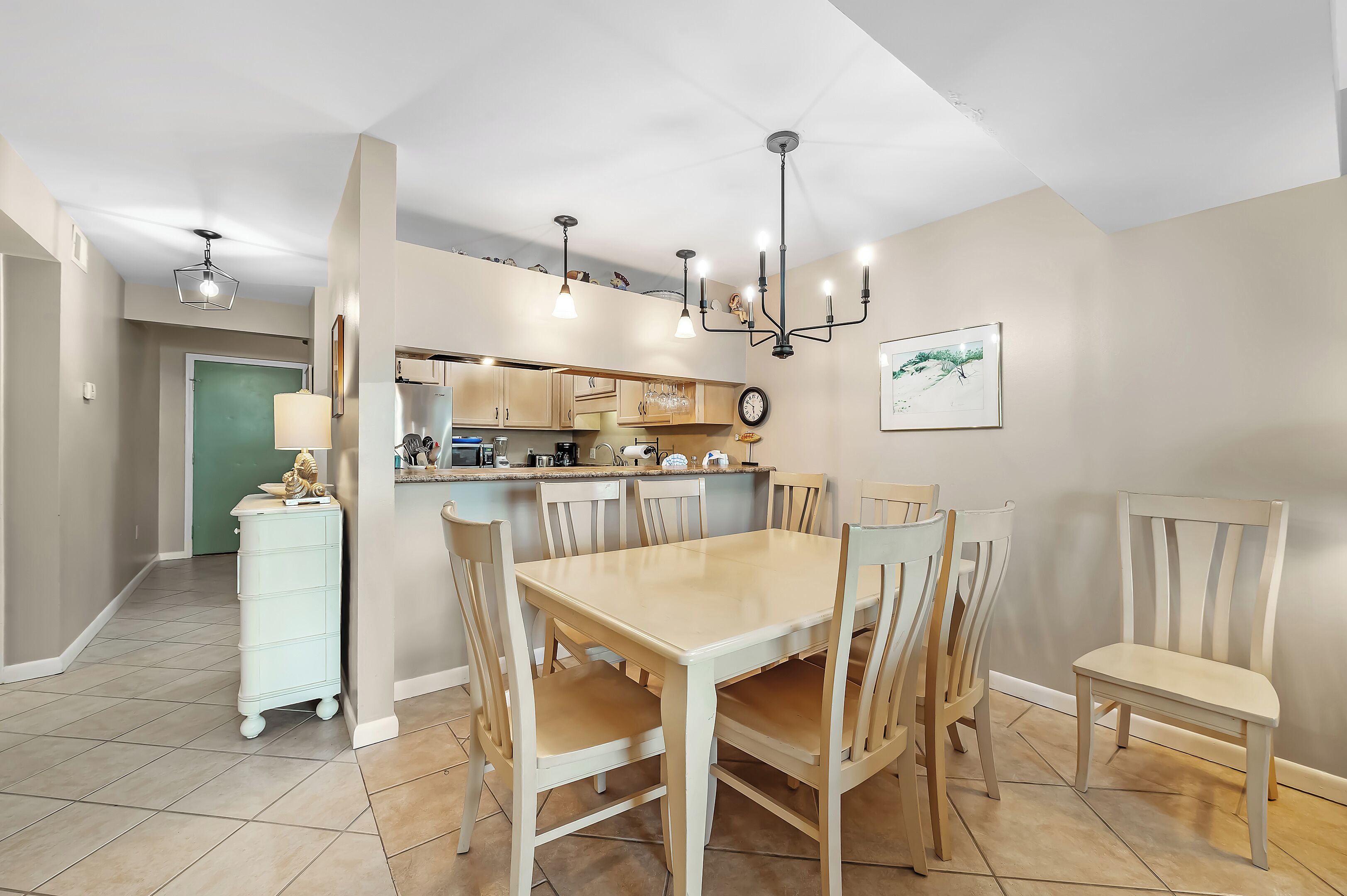 Un'area pranzo con tavolo e sedie in legno, una cucina sullo sfondo e un lampadario.